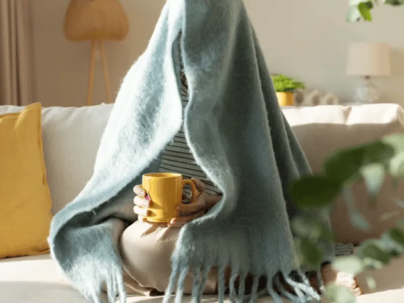 Nainen juomassa teetä peiton alla.